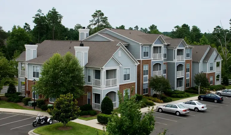 light-blue-and-brown-apartment-block-with-parking-lot-and-trees-in-background