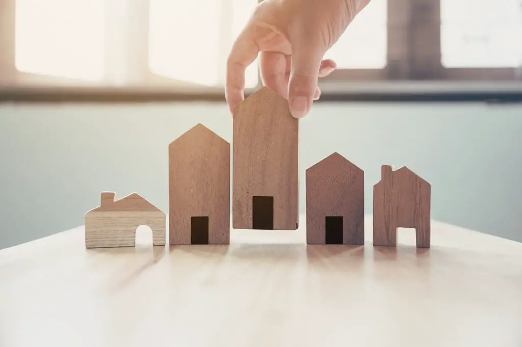 hand-placing-wooden-house-models-in-a-row-on-table-near-windows