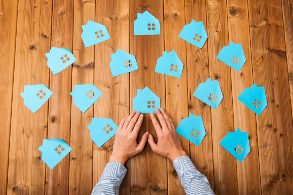 hands-touching-array-of-blue-paper-houses-on-wooden-table