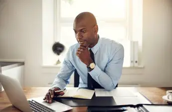 landlord-sitting-at-desk-with-laptop-and-papers-while-looking-at-tenant-screening-reports-online